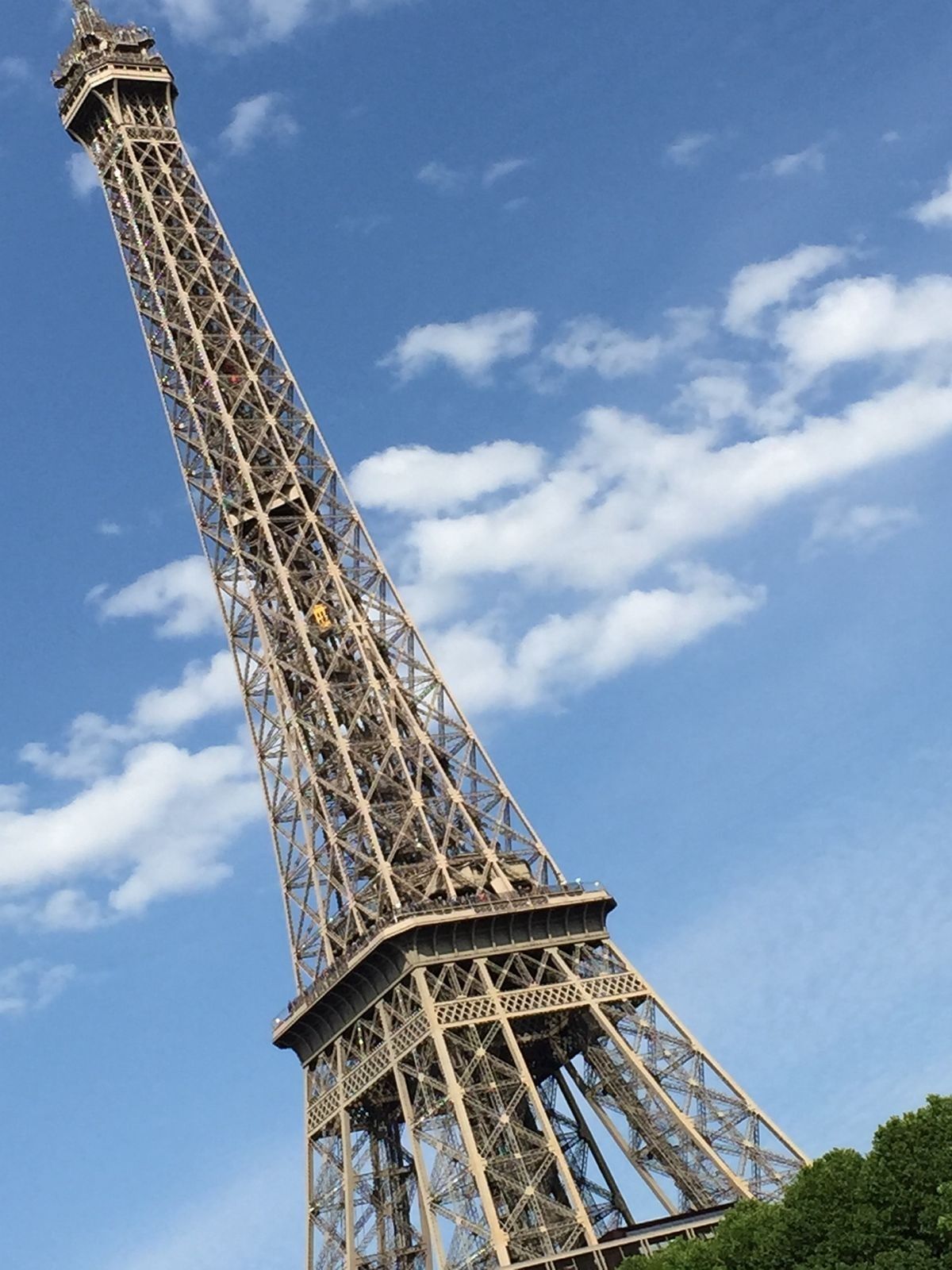 The Eiffel Tower seen from below against a blue sky with scattered clouds