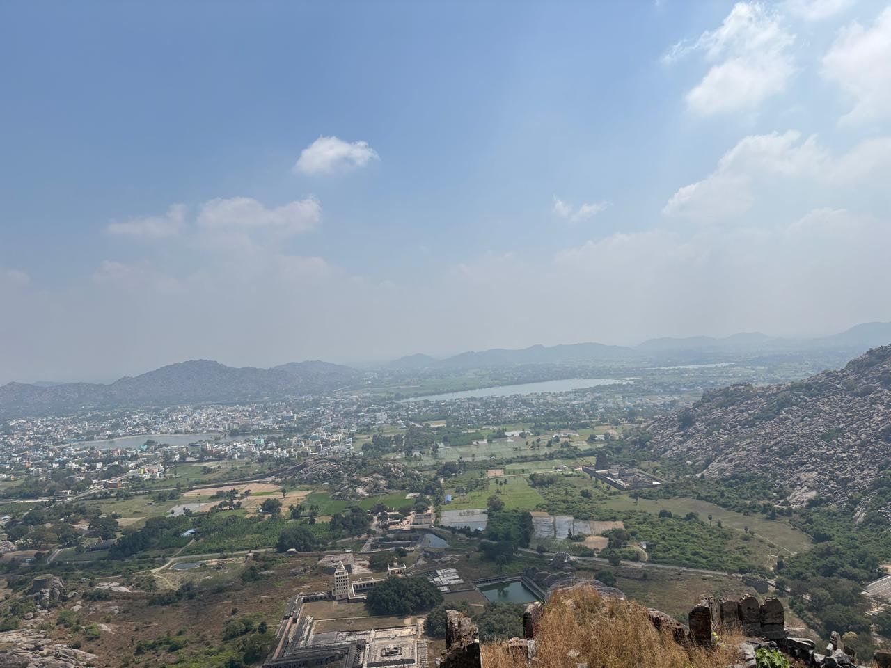 A hazy hilltop view over a town, green fields and a lake, with old stone walls in the foreground